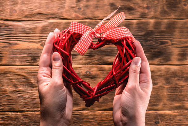Female hand is holding a red heart gift on the brown wooden table background. - Foto, immagini