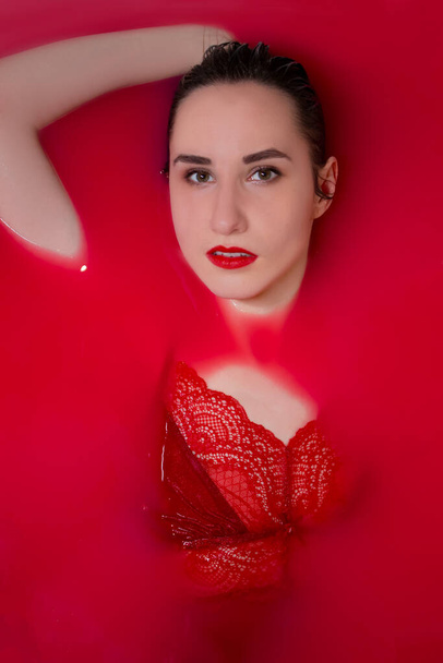 portrait of a beautiful brunette in red lingerie in red water. horror films. Photoshoot in the bathroom. copy space - Foto, Bild