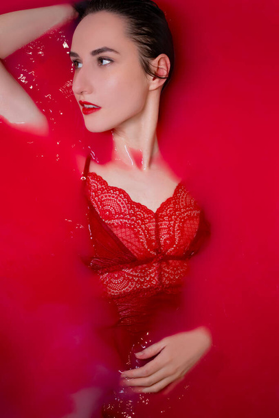 πορτρέτο μιας όμορφης μελαχρινής με κόκκινα εσώρουχα σε κόκκινο νερό. ταινίες τρόμου. Φωτογράφηση στο μπάνιο. αντίγραφο χώρου - Φωτογραφία, εικόνα