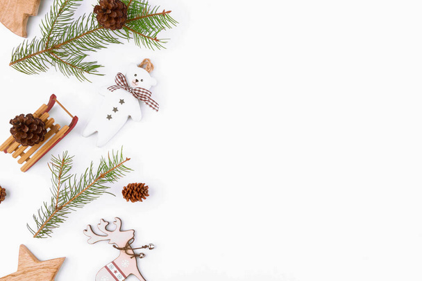 Рождественский фон еловых ветвей, деревянные нулевые отходы домашнего убранства: сани, конус, северный олень, звезды на белом фоне, вид сверху. Многоразовый устойчивый переработанный декор. Экологически чистый новый год - Фото, изображение