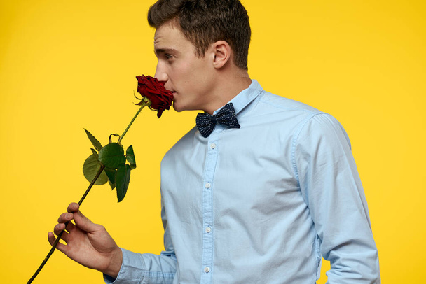 Eleganter Mann im Anzug mit roter Rose in den Händen auf gelbem Hintergrund, abgeschnittene Ansicht - Foto, Bild