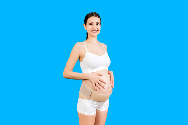 Retrato de una mujer embarazada en ropa interior con vendaje elástico contra el dolor en la espalda al fondo azul con espacio para copiar. Concepto de cinturón de soporte abdominal ortopédico. - Foto, Imagen