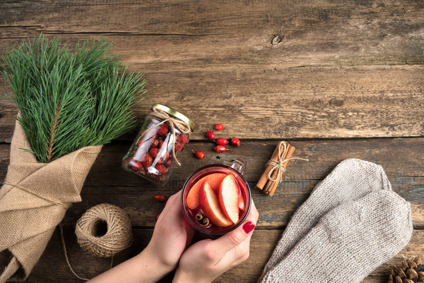 Weihnachtlicher Hintergrund mit einem Strauß Tannenzweige und einem Glas Glühwein in Frauenhand auf einem hölzernen Hintergrund. - Foto, Bild