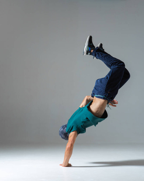Cool guy breakdancer stands on hands dancing in studio isolated on gray background. Dance school poster - Foto, Bild