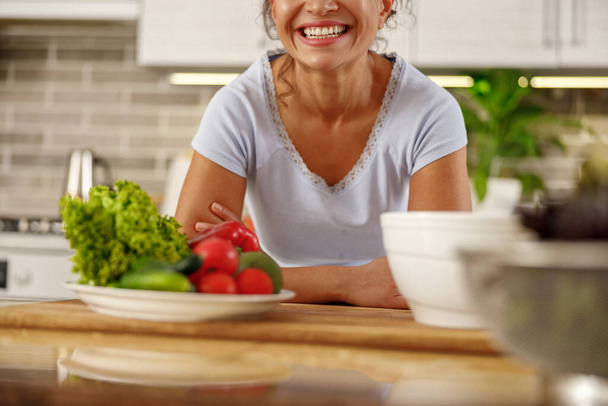 Beautiful smily handsome woman is preparing tasty fresh healthy salad at her kitchen at home - Фото, зображення