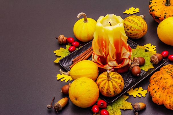 Autumn composition for Thanksgiving or Halloween. Burning carved candle, ripe pumpkins, acorns, fall leaves and rosehip berries. Stone concrete background, copy space - Photo, Image