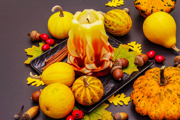 Autumn composition for Thanksgiving or Halloween. Burning carved candle, ripe pumpkins, acorns, fall leaves and rosehip berries. Stone concrete background, close up - Photo, Image