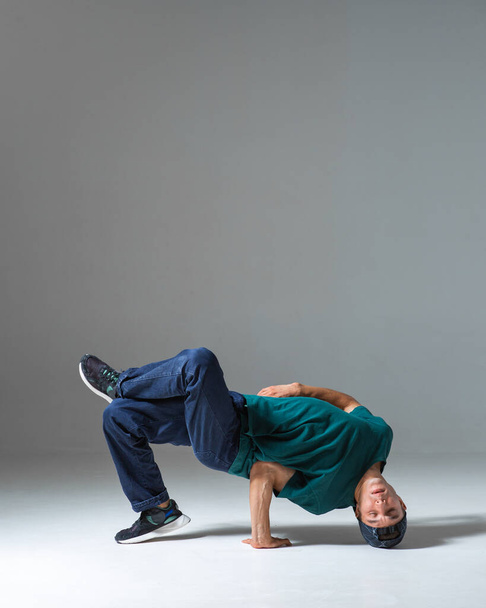 Young guy breakdancer dancing on the floor isolated on gray background. Breakdance lessons - Photo, Image