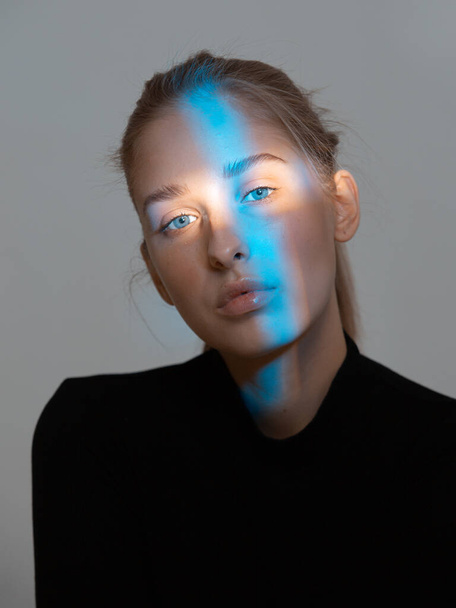 Stylish beautiful young girl with a blue light on her face. Beauty portrait - Valokuva, kuva