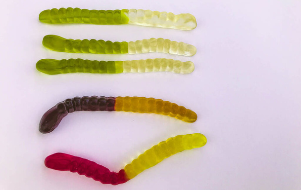 gummy worms lie on a white matte background. bright, mouth-watering gelatinous worms of different colors. worms are stacked in rows, according to colors, from light to dark - Photo, Image