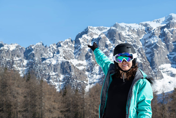 Egy nő színes síöltönyben, sisakban és napszemüvegben síelés után a hegycsúcsok hátterében áll. Sport koncepció, emberek, utazás - Fotó, kép