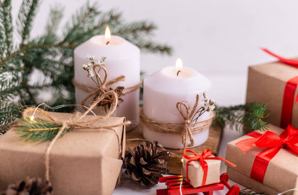 Composición navideña. Velas ardientes y guirnalda, ramas de abeto, regalos y cinta. Fondo rústico blanco. - Foto, Imagen