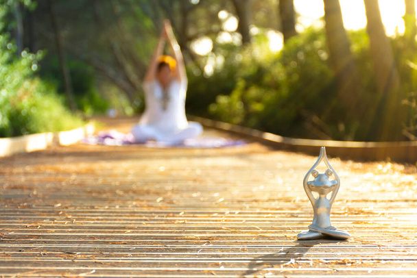 Retroilluminazione di una figura rana yoga in primo piano e una donna sfocata sullo sfondo sia in posa loto meditando con le mani sopra la testa, al tramonto - Foto, immagini
