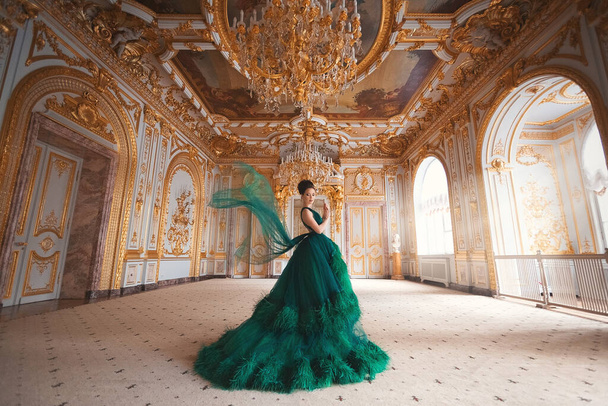 Retrato de una hermosa joven en un vestido verde de alta costura de pie en un lujoso interior de oro. - Foto, imagen