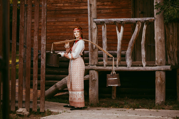 Beautiful Slavic girl with long blonde hair and brown eyes in a white and red embroidered suit and a yoke on her shoulders.Traditional clothing of the Ukrainian region.summer day - Φωτογραφία, εικόνα