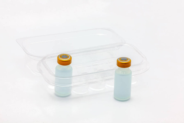 Twee vaccinflesjes één binnen en één buiten een open doorzichtige plastic doos voor tien vaccinflesjes - Foto, afbeelding