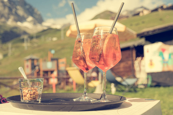 Pair of wine glasses filled with refreshing orange cocktail at mountain resort. - Photo, Image