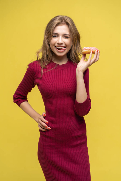 Beautiful young woman tasting colorful donut. Studio portrait over yellow background. - Φωτογραφία, εικόνα