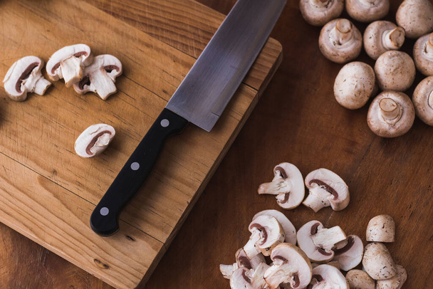 gesneden champignon op een snijplank met een mes - Foto, afbeelding