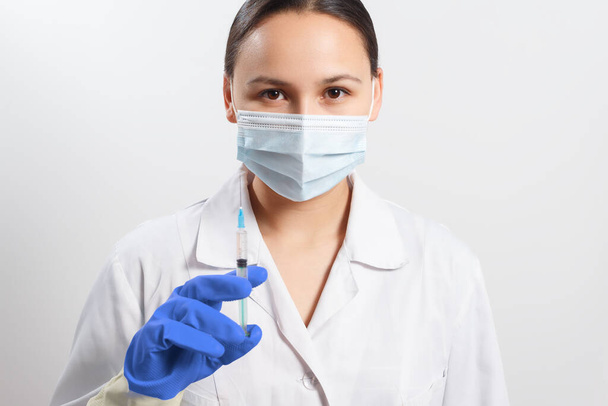 doctor in gloves and a protective mask with a syringe. vaccination against coronavirus covid-19 - Photo, image