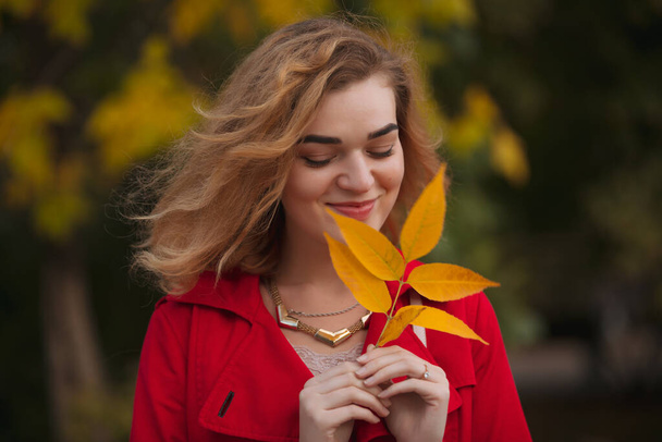 Portrait of woman in red coat holding yellow autumn leaf - Foto, Imagen