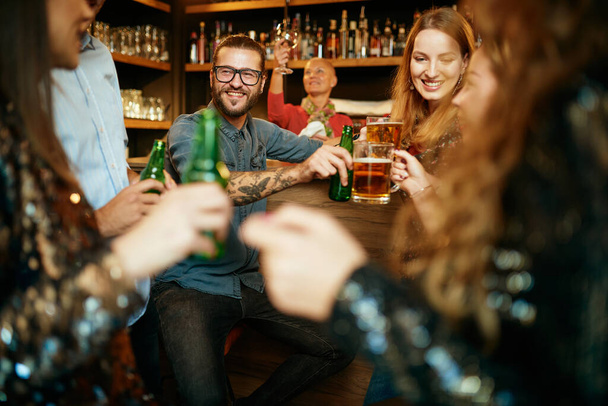Groep beste vrienden zit in een pub, chatten en toasten met bier. - Foto, afbeelding