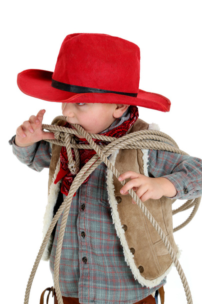 Bonito jovem cowboy criança mordendo uma corda usando chapéu vermelho
 - Foto, Imagem