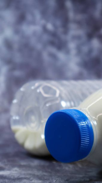 Eine Plastikflasche mit frischer normaler Milch auf dunkelgrauem Marmor oder Beton. Nahaufnahme von vorne. Weltmilchtag-Konzept. Nährflüssigkeit. Vertikale Fotografie - Foto, Bild