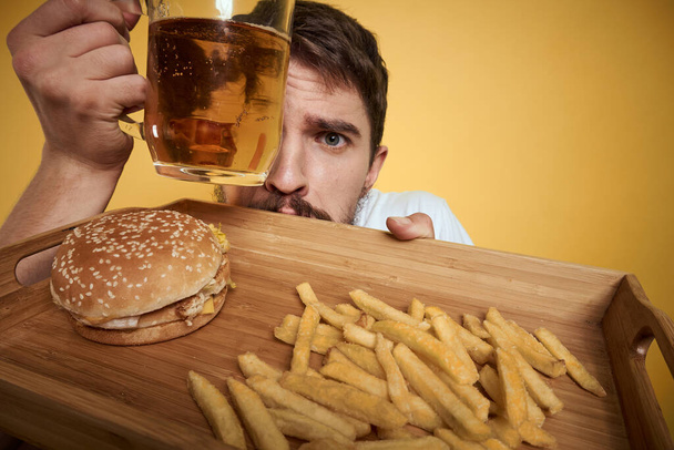 Barbudo hombre con taza de cerveza comida rápida dieta diversión alcohol estilo de vida amarillo fondo - Foto, Imagen