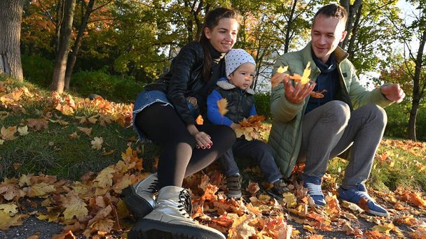 Maman, papa et leur petit enfant jettent des feuilles dans un parc d'automne. Photo de haute qualité - Photo, image