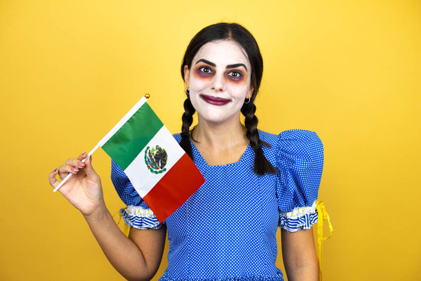 kobieta nosi straszny kostium halloween lalki na żółtym tle trzymając flagę Meksyku - Zdjęcie, obraz