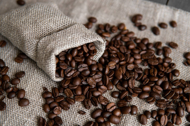 Coffee scattered from a linen bag. Fresh arabica coffee beans on linen textile. - Foto, Imagen