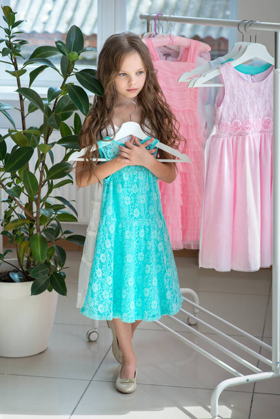 Little child girl choosing her clothes. Kid thinking what to choose to wear in front of many choices of dresses on hangers. Sales, buy and sell concepts. - Фото, зображення