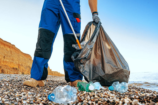 Close up photo of a man collecting garbage with a grabbing tool on the beach - Foto, afbeelding