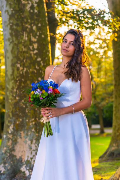 Portrait Caucasian brunette in wedding dress at wedding celebration with bouquet of colorful flowers - Фото, изображение