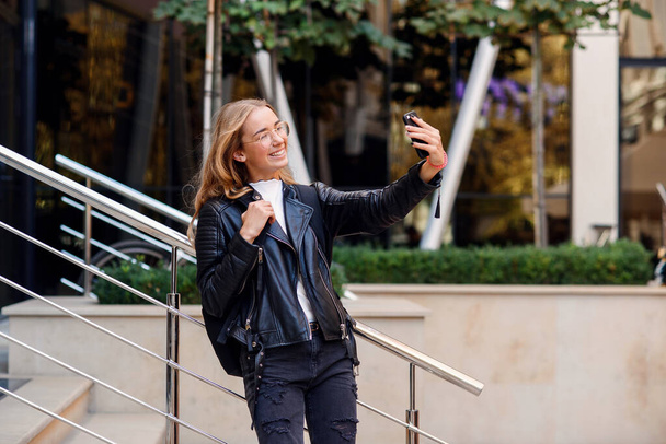 Cheerful beautiful student girl has online video conversation on smart phone on the street, enjoying walk outdoors. - Fotoğraf, Görsel