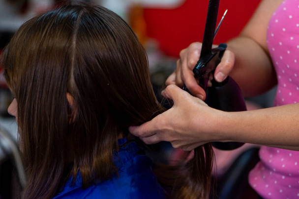 Szakmai female hairdresser cutting girl 's brown hair in salon, closeup - Fotó, kép