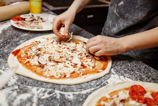 Μαγειρέψτε στην κουζίνα βάζοντας τα υλικά στην πίτσα. Σχέδιο πίτσας. Παραγωγή και παράδοση τροφίμων. - Φωτογραφία, εικόνα