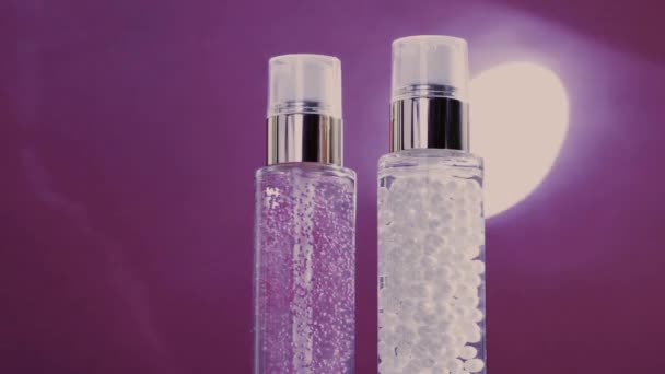 Make-up základna a sérum gel jako luxusní výrobky pro péči o pleť a lesklé světelné erupce na fialovém pozadí, péče o pleť rutina pro kosmetiku obličeje a kosmetické značky - Záběry, video
