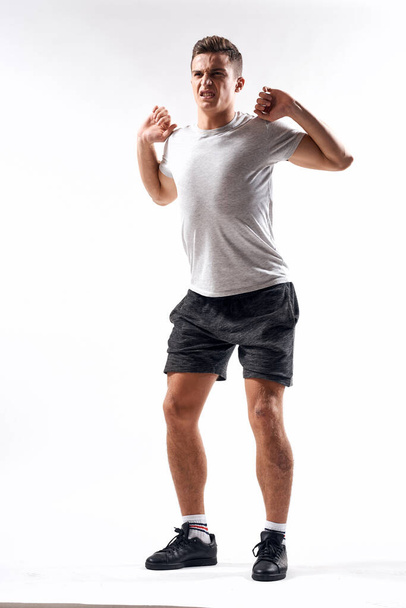 Спортивный человек в шортах и футболке делает упражнения на светлом фоне - Фото, изображение