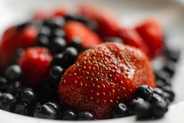 Многие сочные свежие красные ягоды и ежевики лежат на белой керамической тарелке на столе - Фото, изображение
