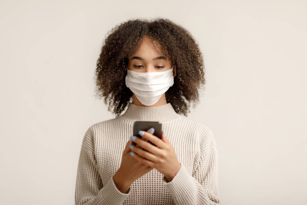 Blog moderno sobre saúde e epidemia de coronavírus. Africano mulher americana mensagens de texto no smartphone sobre quarentena - Foto, Imagem