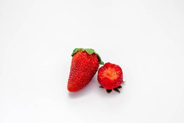 2 fresh, organic strawberries isolated on a white background. One berry has a bite from it. - Фото, изображение