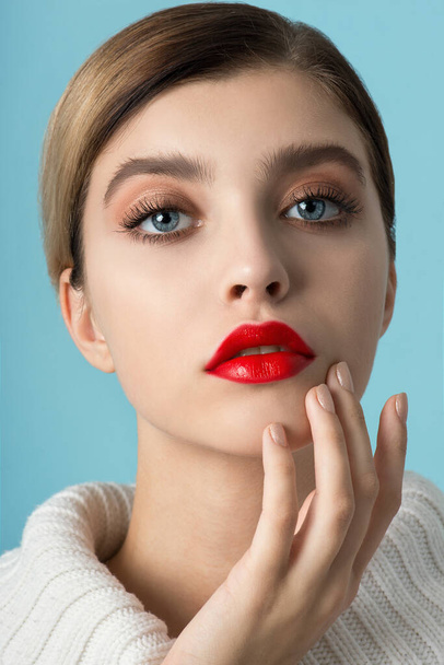 Portrait of beautiful young woman with perfect young skin, red matt lips in white fur.  Model with bright scarlet color makeup and sparkled manicure posing on light blue background. Winter seasonal beauty concept. Close up, copyspace. - Foto, Imagem