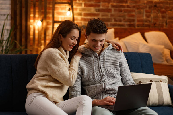Winter holidays, Christmas celebrations, New Year concept. Portrait of beautiful smiling couple watching Christmas movie at home. Beautiful young couple at home enjoying spending time together - Foto, Imagem