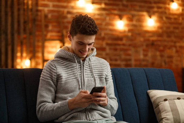 Young freelancer using smartphone and smiling. Happy man using mobile phone apps, texting message, browsing internet, looking at smartphone, sitting at home. Young people working with mobile devices - Photo, image