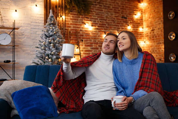 Beautiful young couple at home drinking coffee at Christmas morning. Spending time together, relationships and people concept. Winter holidays, Christmas celebrations, New Year concept - Foto, afbeelding