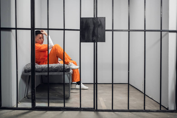 Μοναχικό κελί με έναν εγκληματία με πορτοκαλί ρόμπα σε ασιατική φυλακή. Αντιγραφή χώρου. Θλιβερά συναισθήματα ενός νεαρού.. - Φωτογραφία, εικόνα