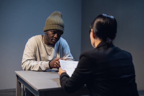 Eine Anwältin mit Brille und ein junger Schwarzer kommunizieren im Verhörraum über die Gründe seiner Inhaftierung - Foto, Bild