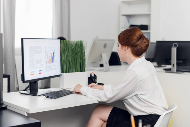 Girl Manager in een witte blouse aan de computer berekent de winst en het verlies van het bedrijf, bouwt grafieken. Monitor model. - Foto, afbeelding